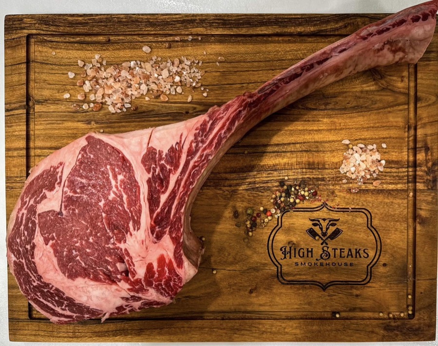 Raw hand-cut tomahawk wagyu ribeye resting on a butcher board
